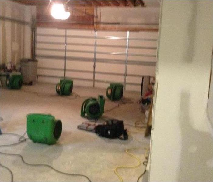 a room that had been damaged by water with green servpro air movers in it 